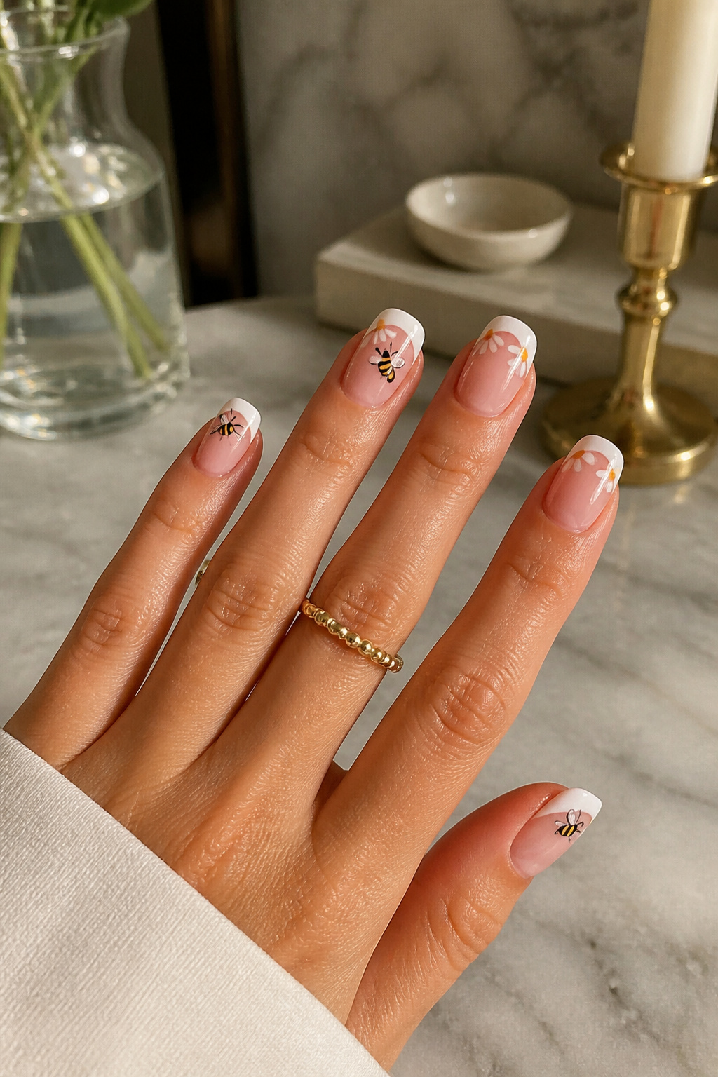 French tip nails featuring tiny black bees and white daisies on a soft pink base.
