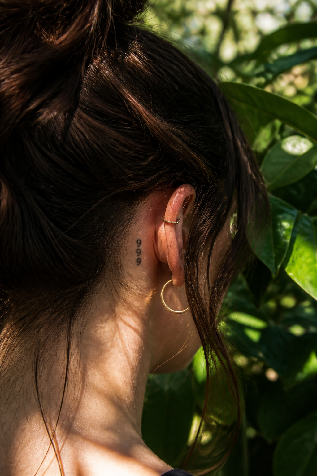 A 999 tattoo placed behind a person's ear in fine line design.