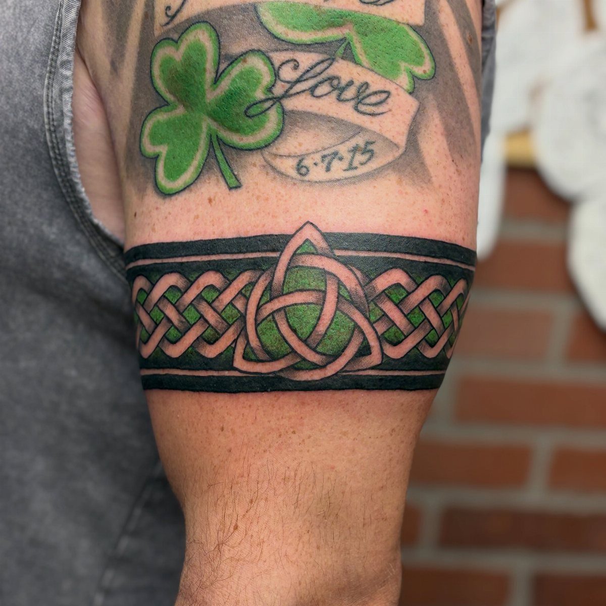 A man's arm featuring a green and black Celtic knotwork armband tattoo.