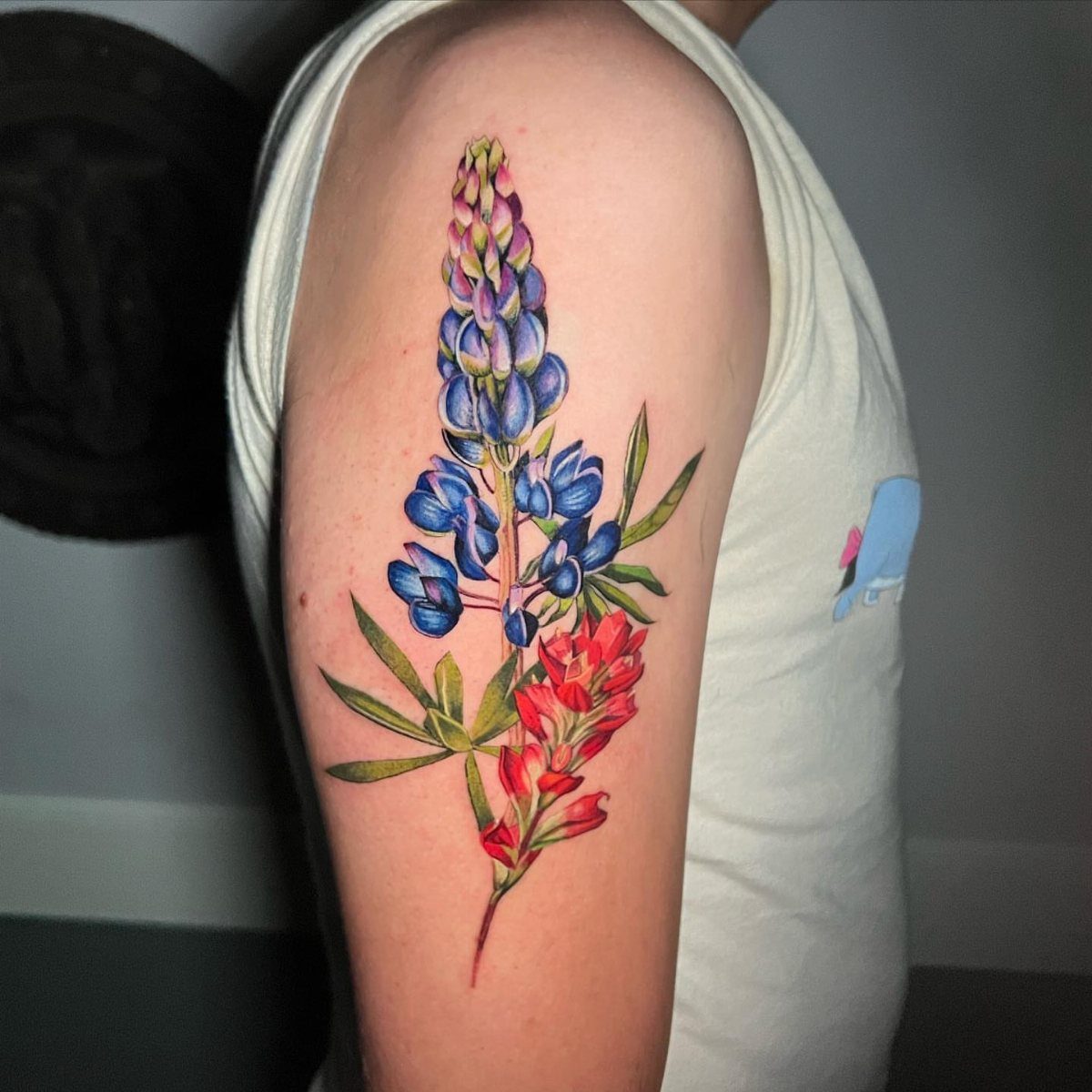 A colorful bluebonnet flower tattoo on a person's upper arm with blue and red petals.