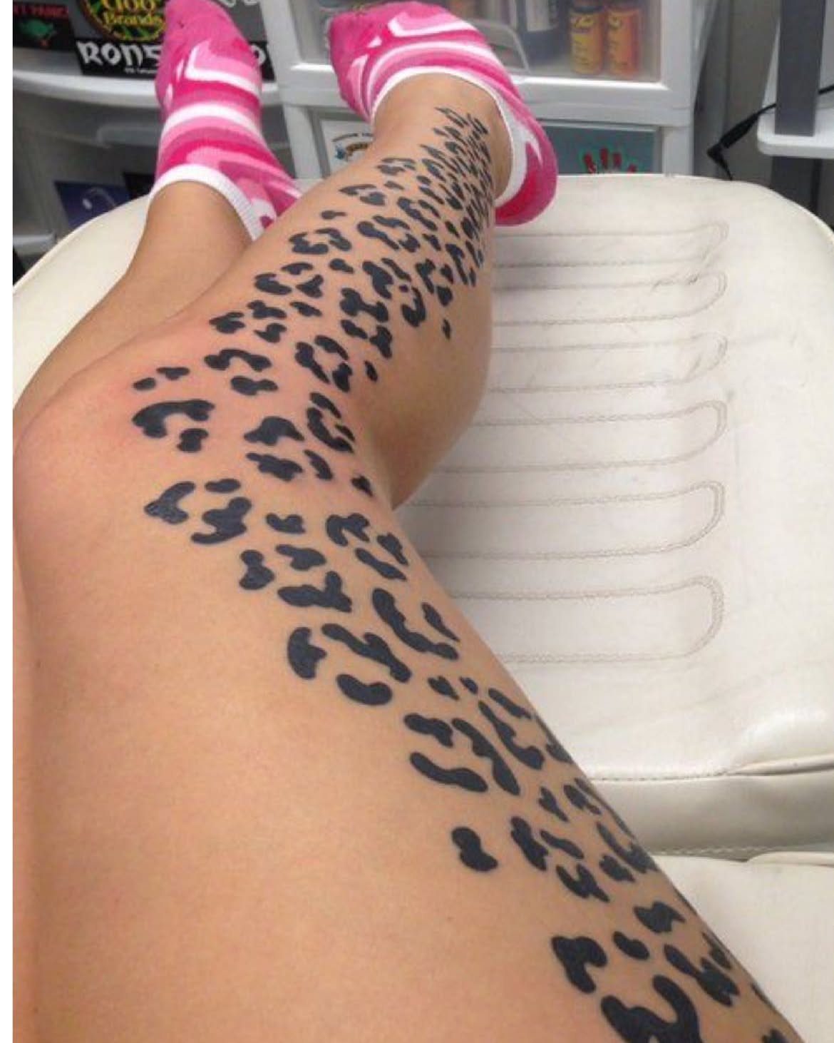 Leopard print tattoo covering a person's thighs and legs while they lie on a white surface.