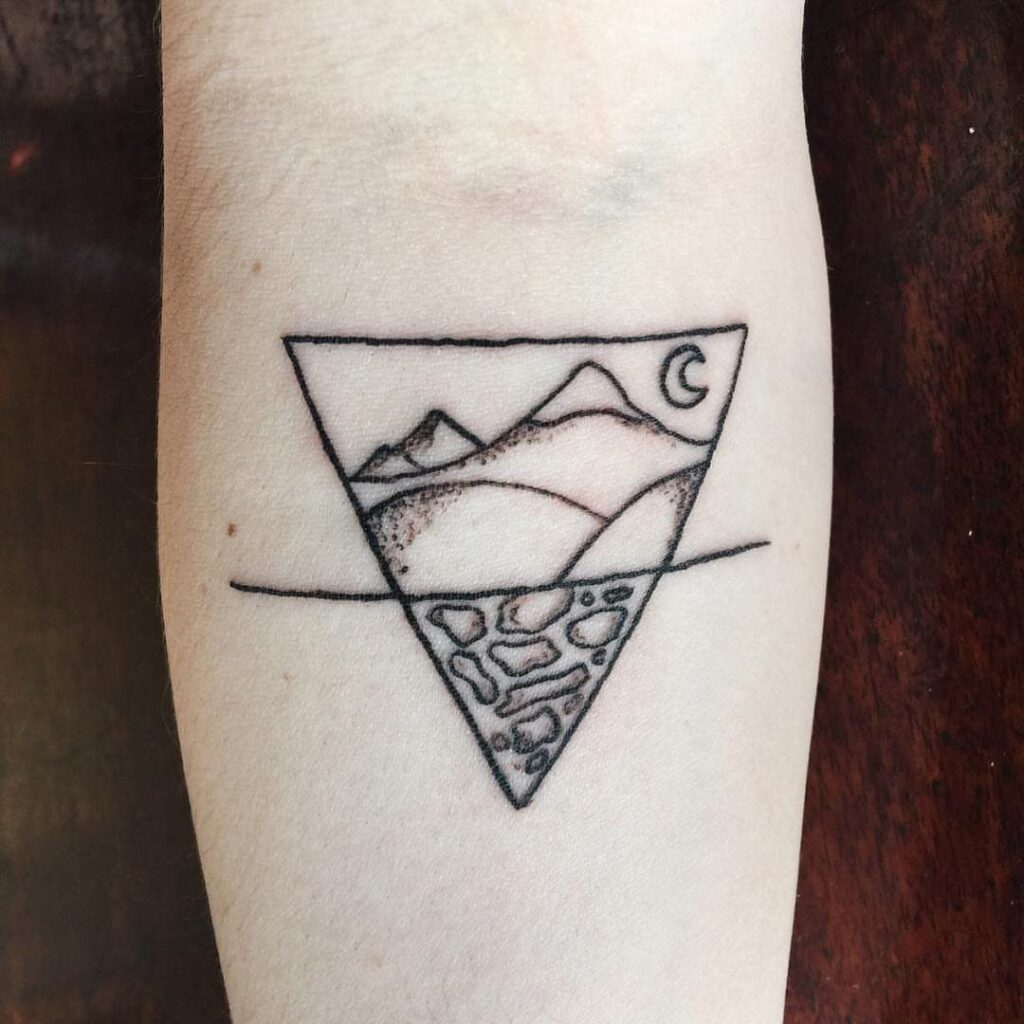 A minimalist black ink tattoo of a mountain landscape and stones inside an inverted triangle.