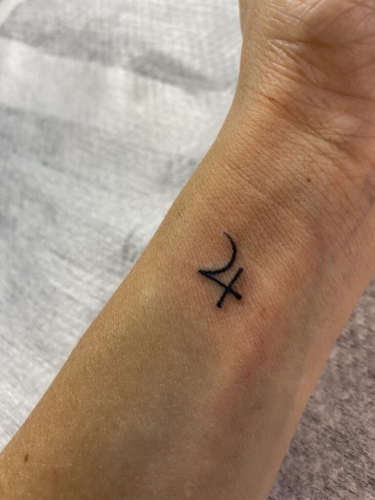 A small black ink Jupiter symbol tattoo on a person's inner wrist.