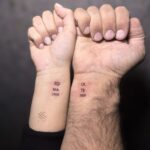 Two wrists held together showing small black ink tattoos that form the word soulmate.