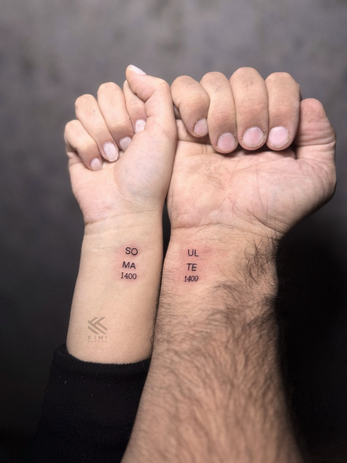 Two wrists held together showing small black ink tattoos that form the word soulmate.