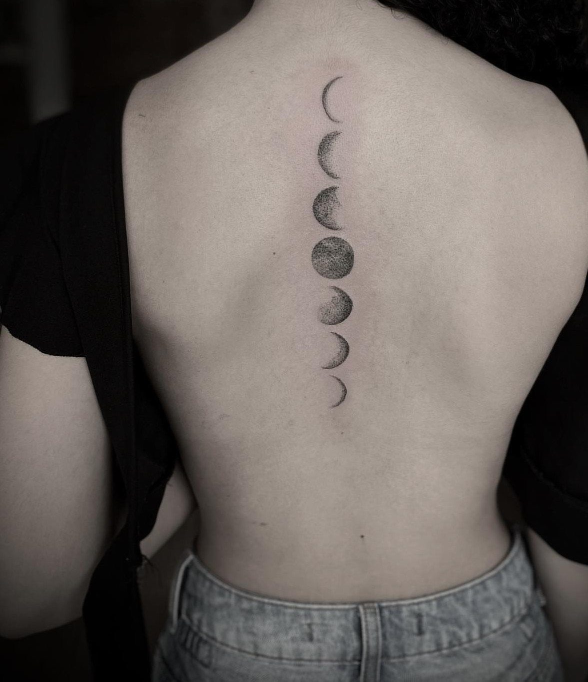 A vertical moon phases tattoo design running down a person's spine.