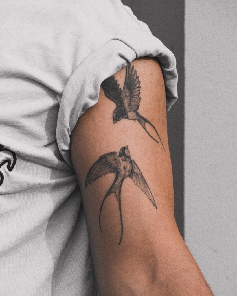 Two black ink swallow tattoos depicted in flight on a person's upper arm.