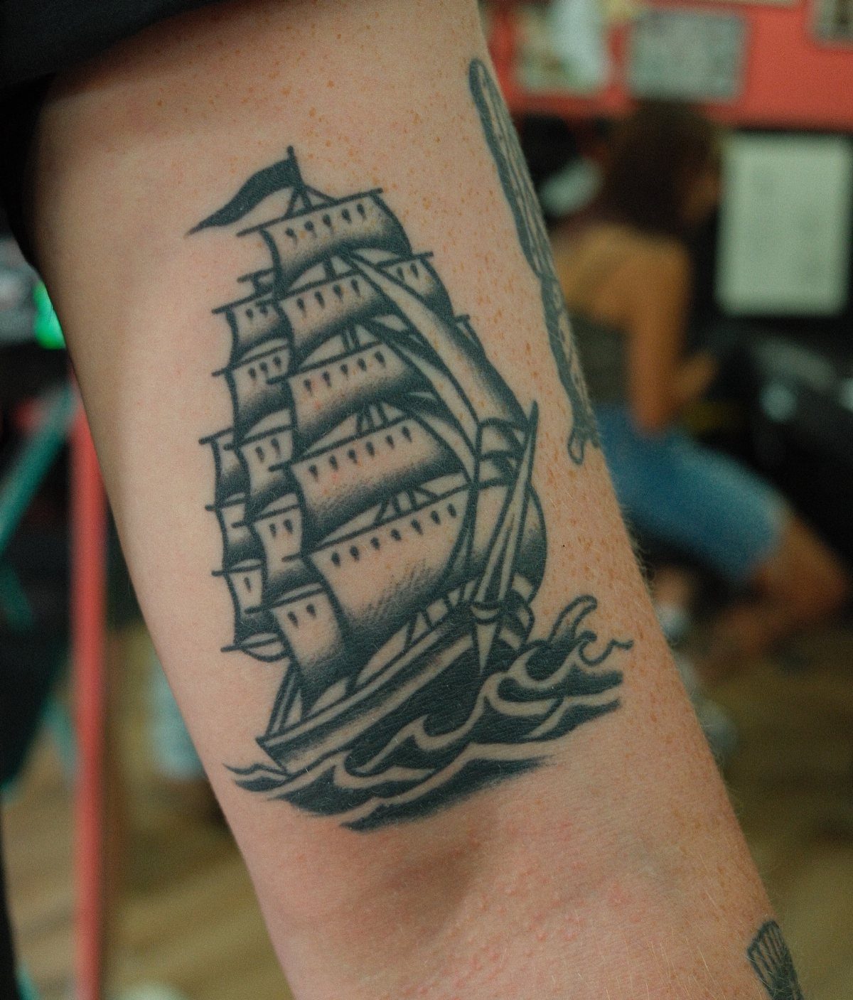 A black ink tattoo of a sailing ship on a person's forearm.