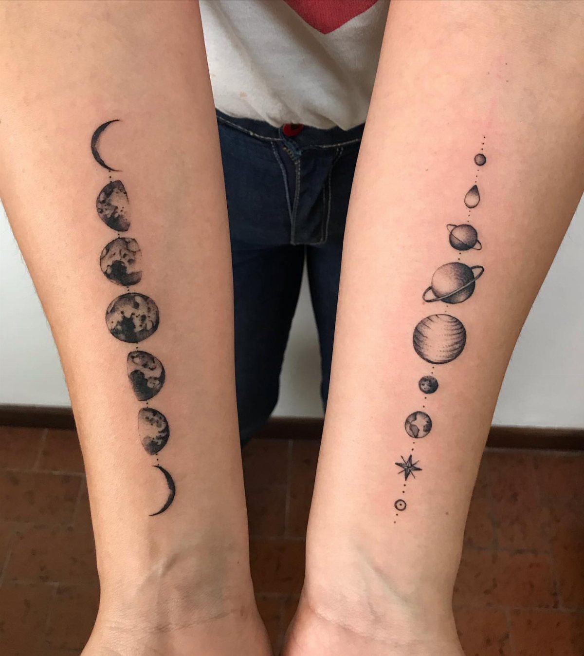 Two forearms displaying vertical black ink tattoos of moon phases and celestial planets.