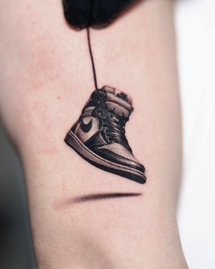 A black and grey realistic tattoo of a high-top sneaker on a person's skin.