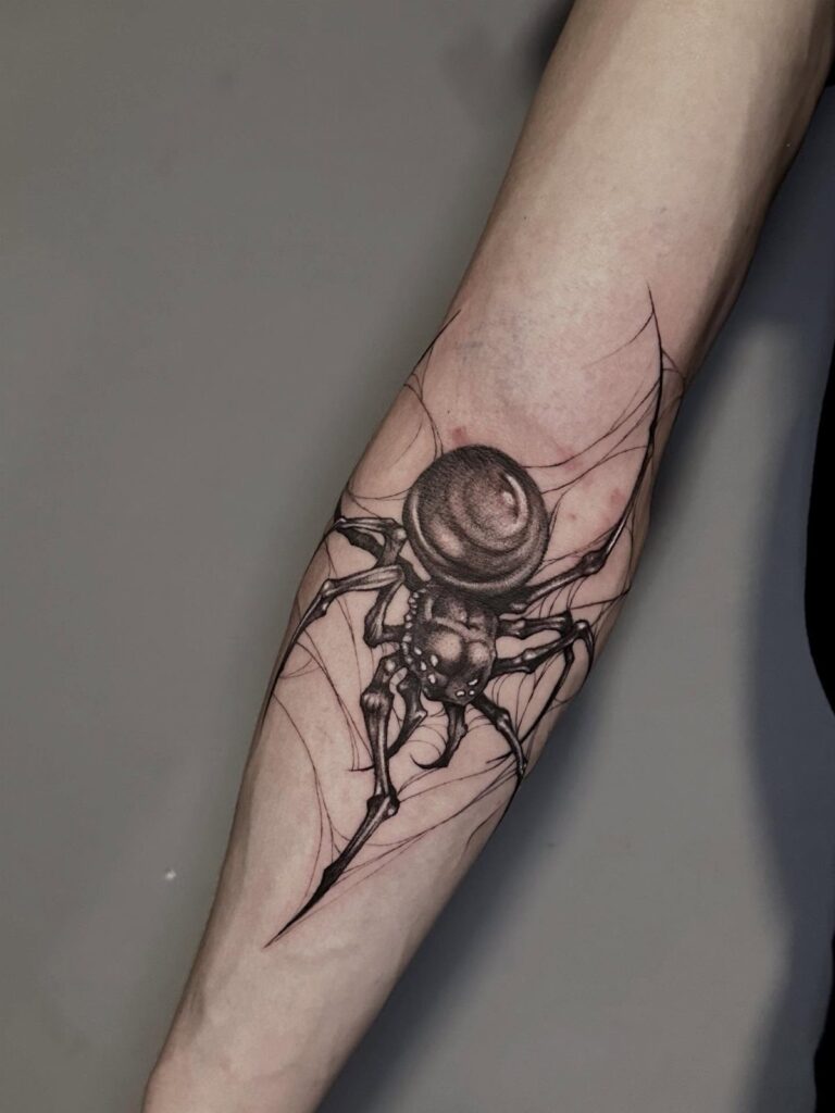 A detailed black and grey spider tattoo with web patterns on a person's forearm.