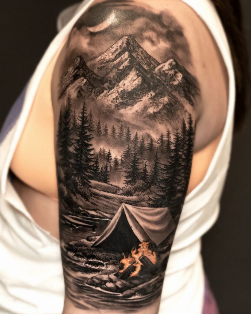 A black and grey mountain landscape tattoo featuring a tent and campfire on a person's arm.