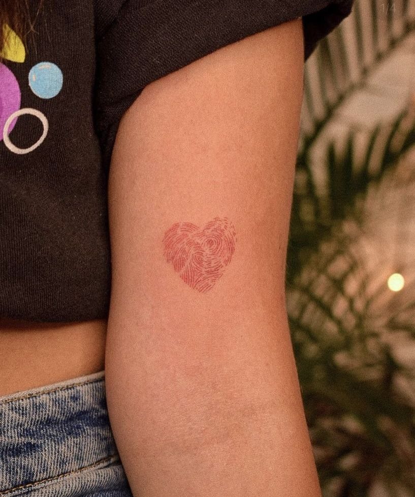 A red heart-shaped tattoo with a fingerprint texture on a person's arm.