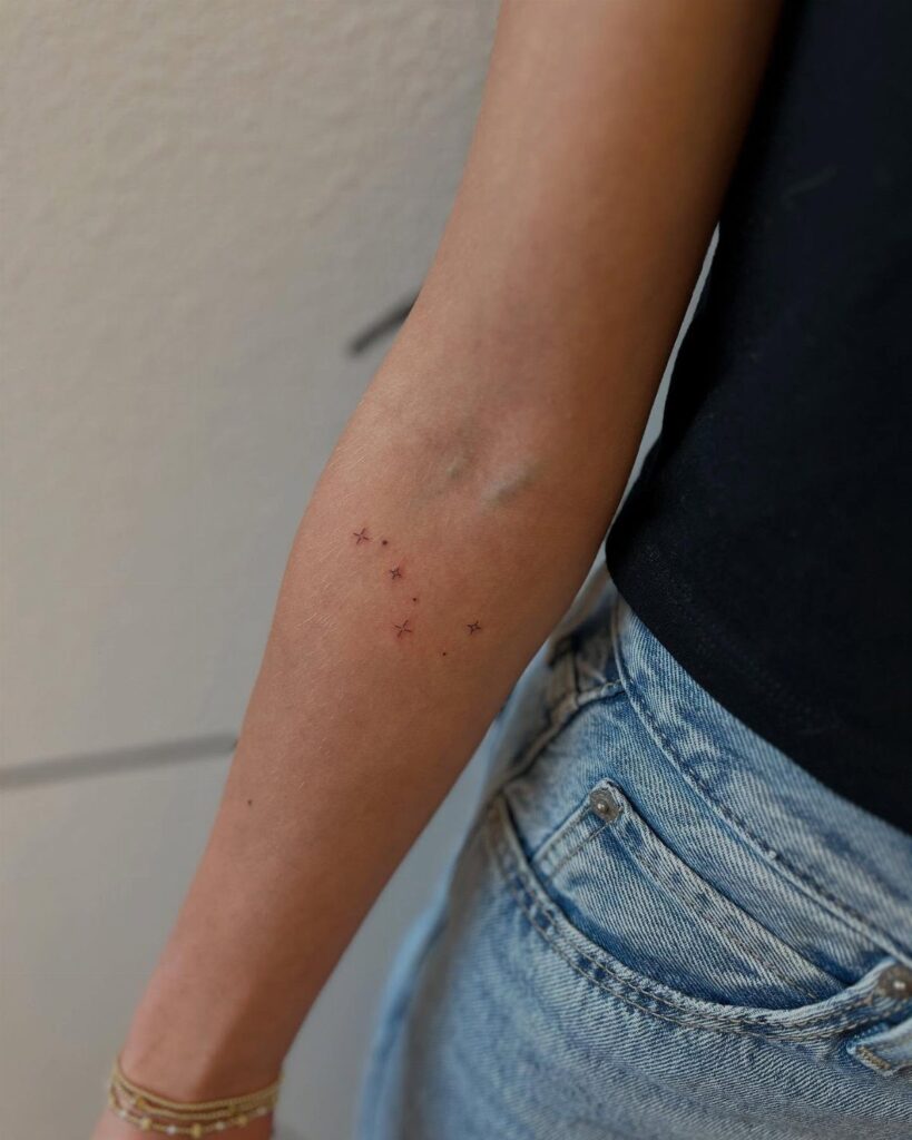 Small minimalist star tattoos scattered in a cluster on a person's forearm.