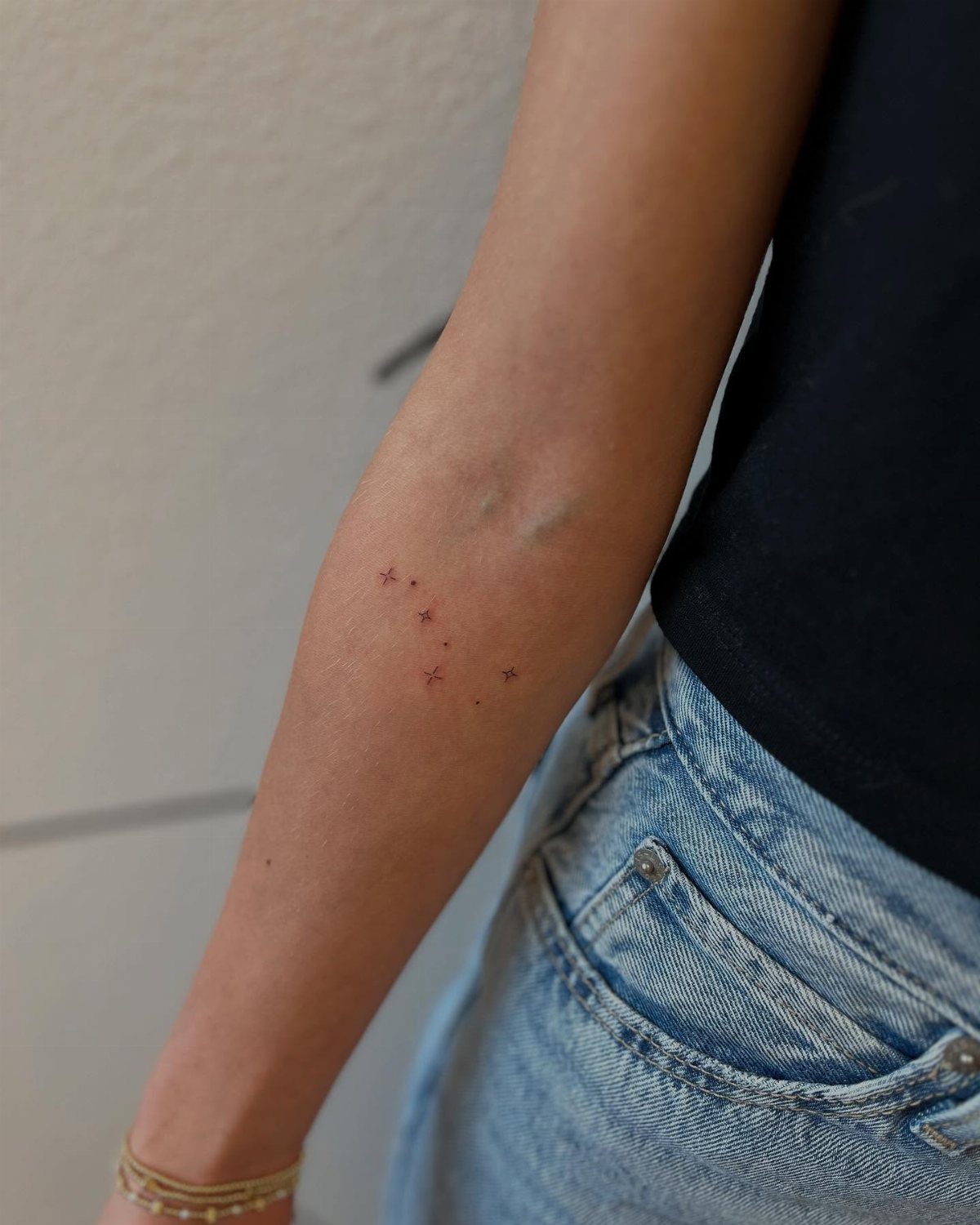 Small minimalist star tattoos scattered in a cluster on a person's forearm.