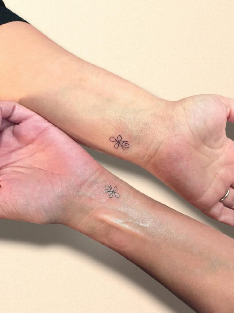 Two wrists held together showing matching small black infinity knot tattoos on the inner skin.